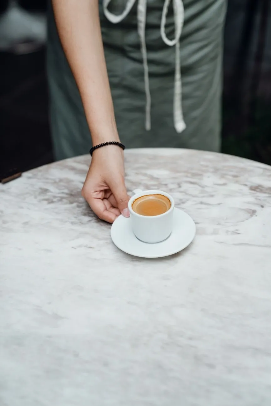A hand setting a small espresso cup on a marble café table