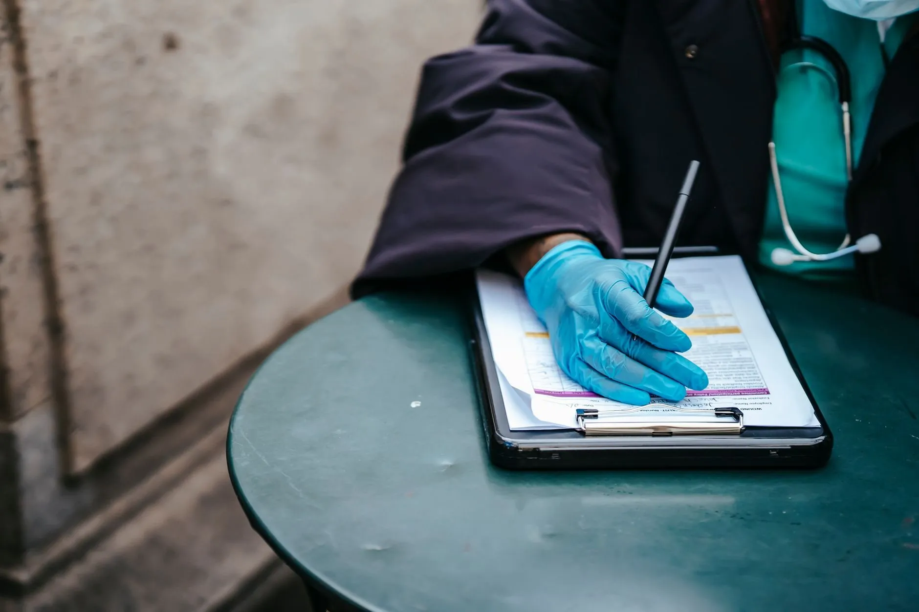 A gloved hand filling in a form on a clipboard at a small round table