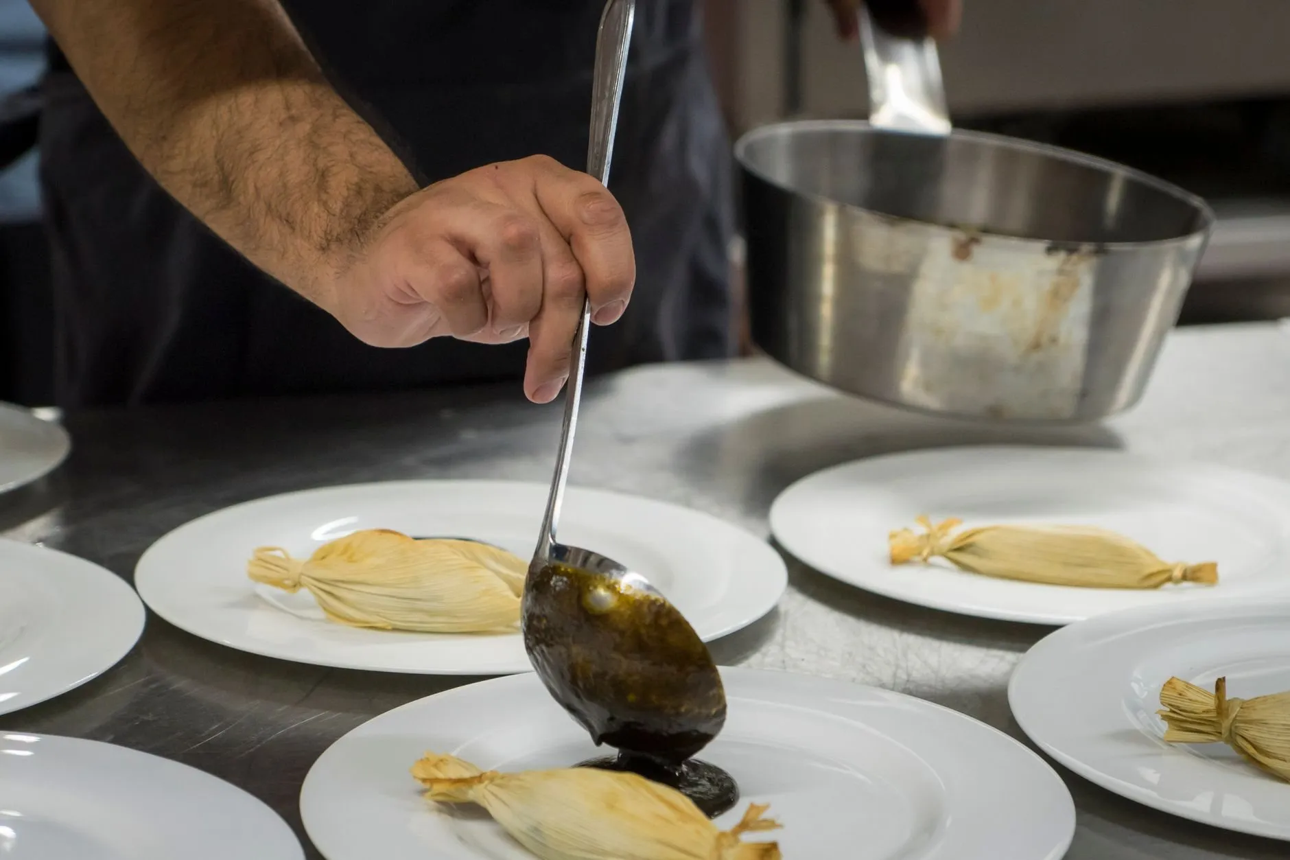 A ladle of sauce poured over plated dishes during service