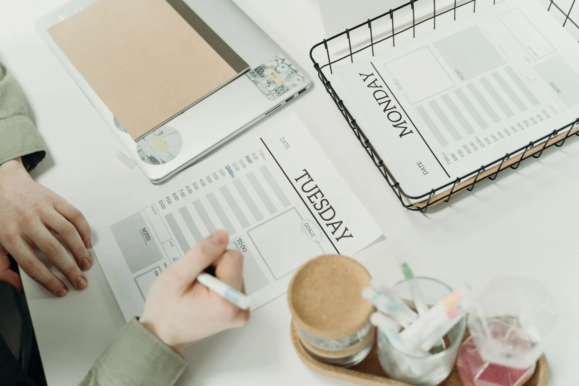 Weekly planner sheets marked Monday and Tuesday on a white desk, with a pen in hand