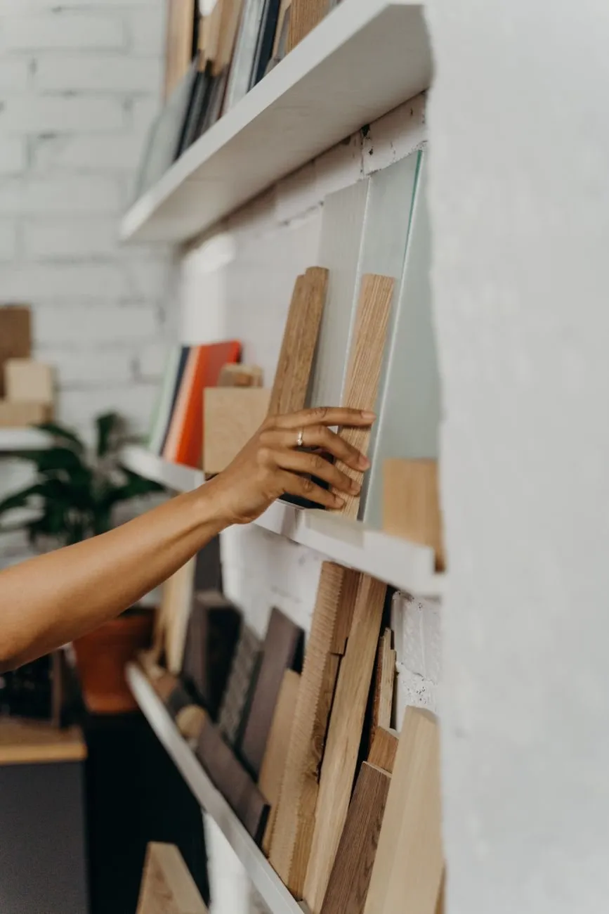A hand arranging wooden boards on a white shop shelf